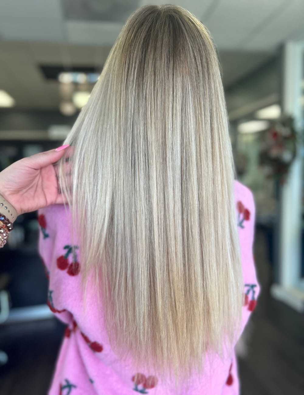 Long, straight blonde hair in a salon, person wearing a pink cherry-patterned sweater.