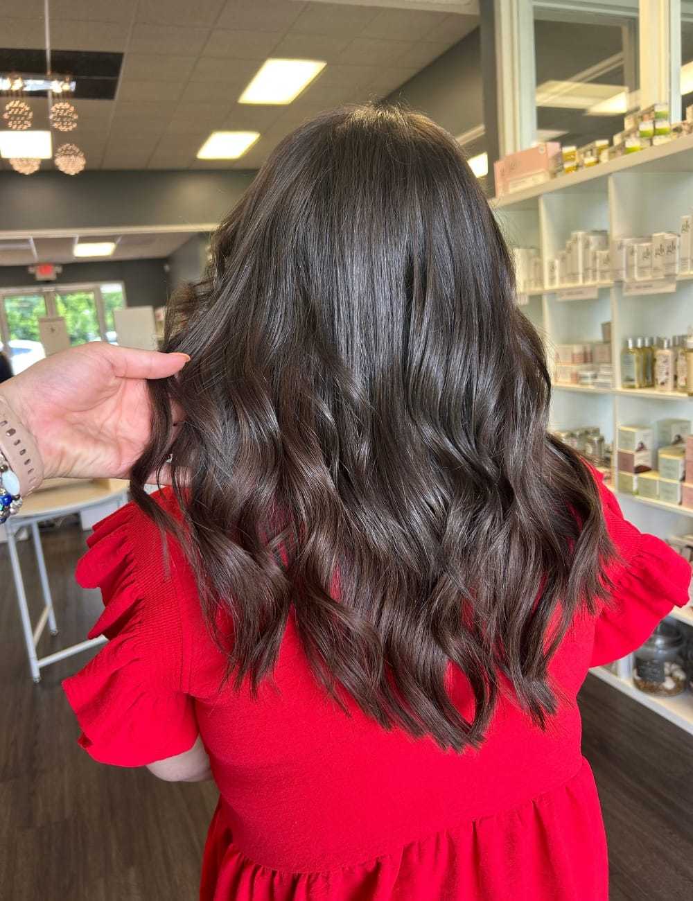 Brunette hair with loose waves, styled in a salon, person wearing a red top.